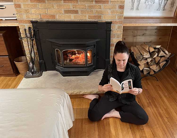 Kelly sits on the floor to read "Meet Your Body" by Noah Karrasch by the fire in her studio.