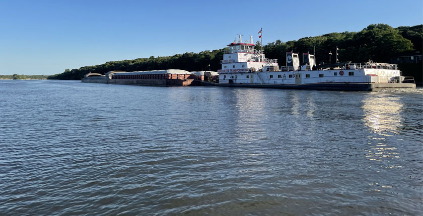 A barge is shown against a backdrop of trees traveling down the Mississippi river.
